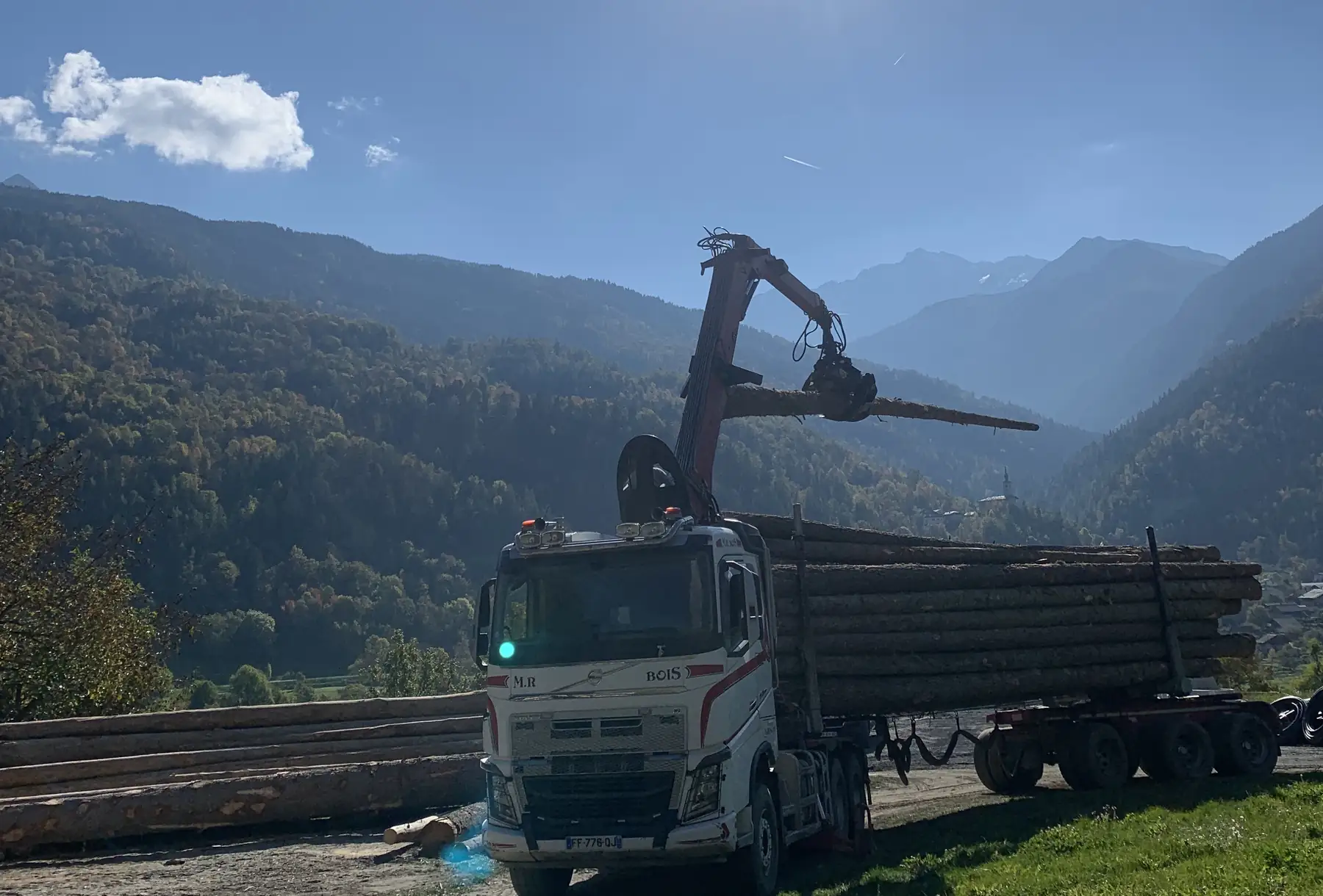 Grumier chargé de troncs de sapin, grue en action, au pied des montagnes de Haute Tarentaise